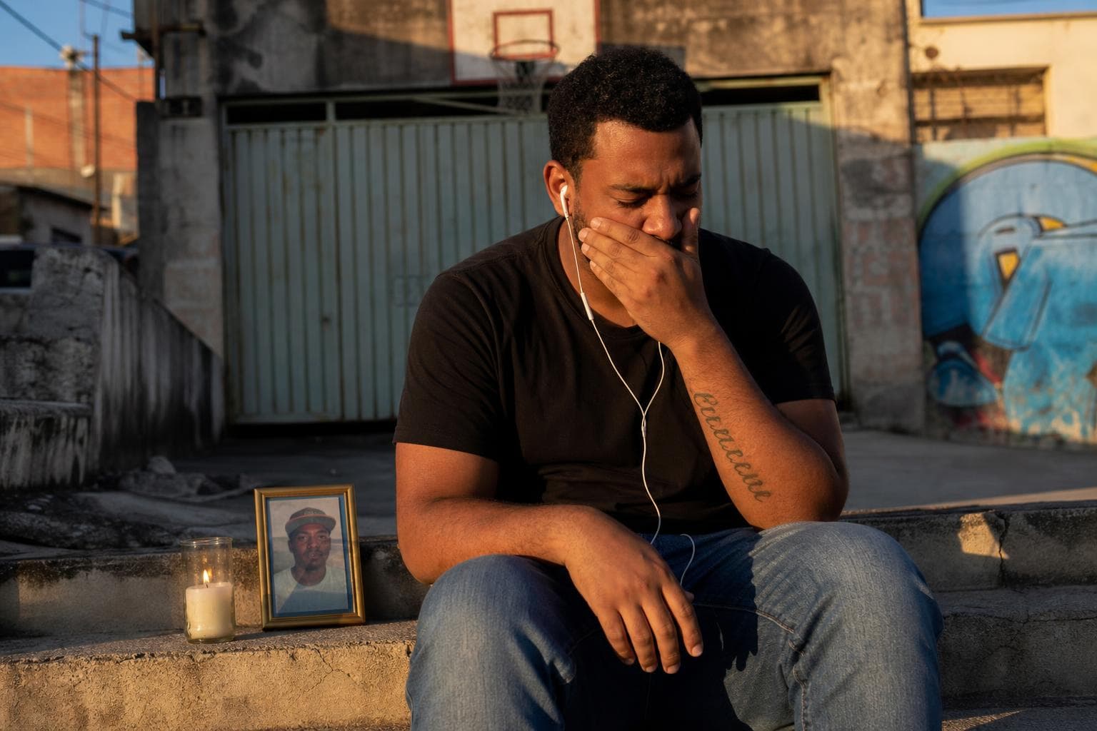 Jovem ouvindo rap de homenagem para o padrinho falecido, sentado na escadaria da quebrada