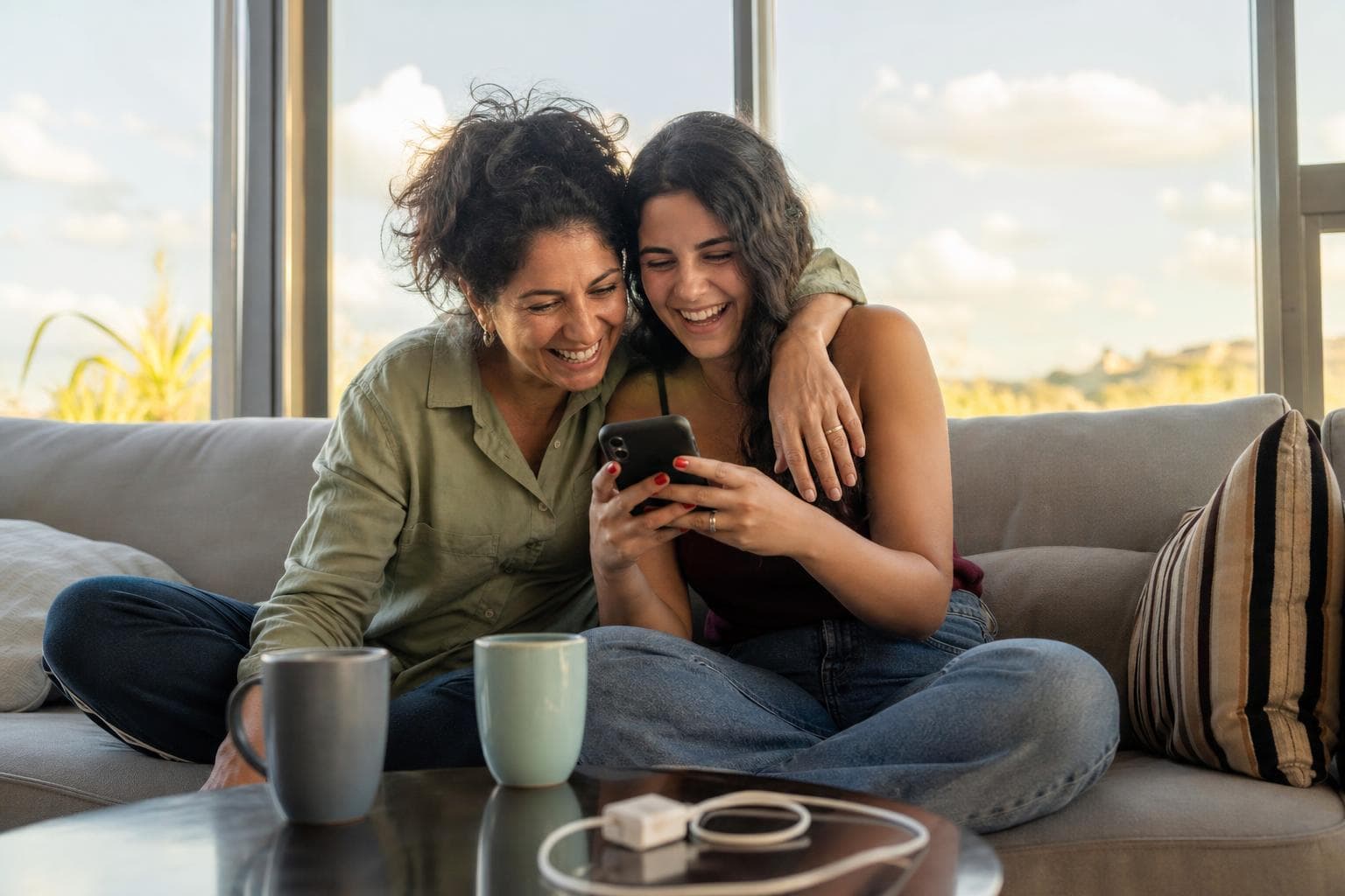 Mãe brasileira jovem e filha adulta juntas como amigas, compartilhando momento descontraído no Dia das Mães