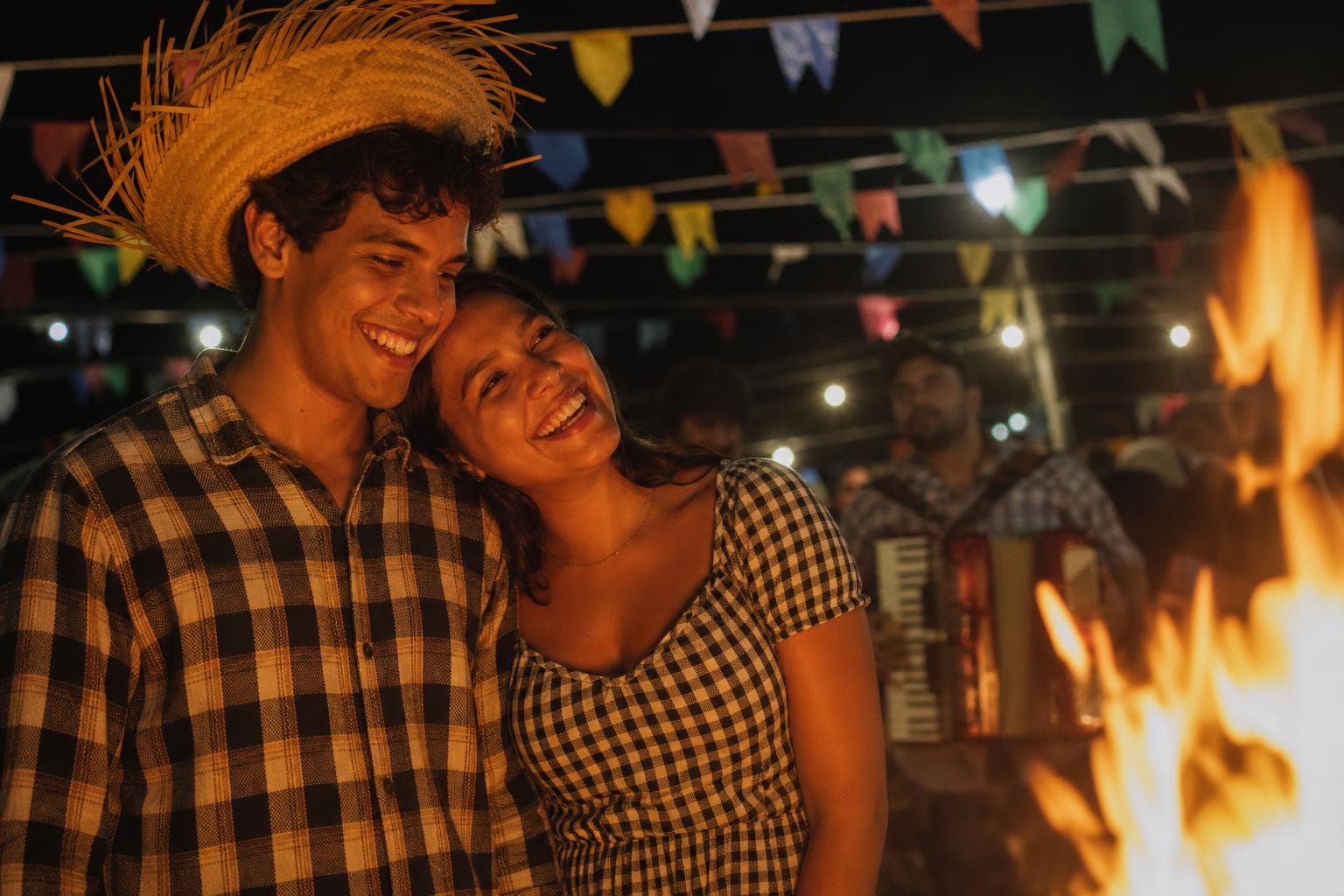 Casal brasileiro dançando forró perto da fogueira numa festa junina, com bandeirinhas e luzes do arraial ao fundo, momento de homenagem personalizada