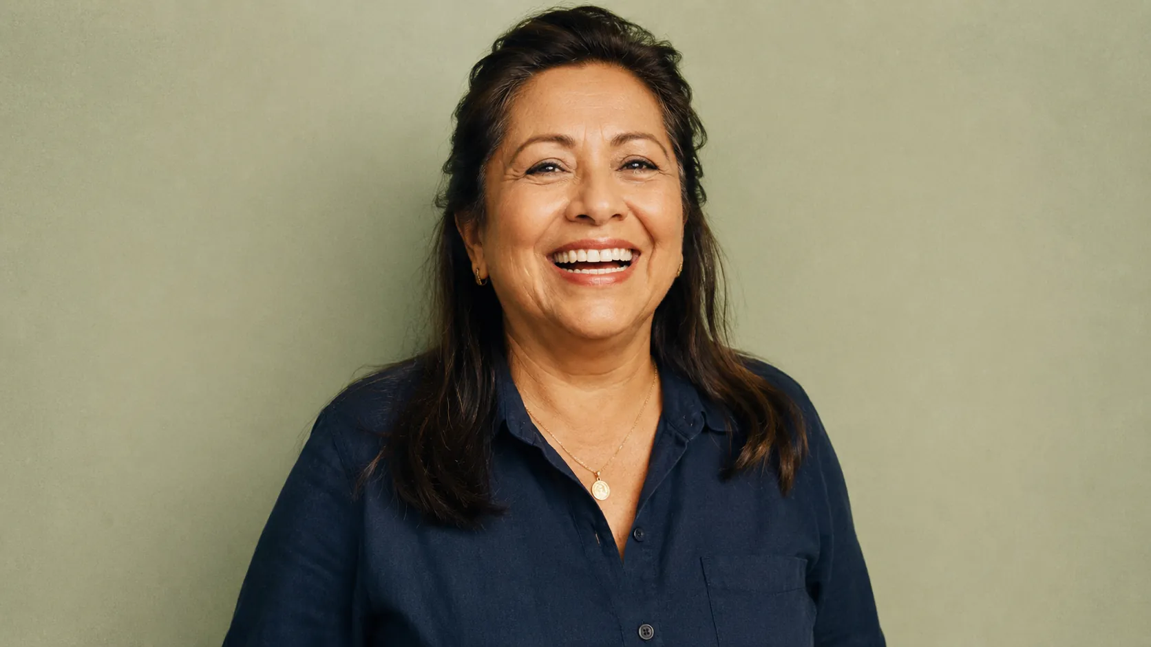 Portrait of Maria — 58-year-old Latina mother in navy shirt, mid-laugh expression